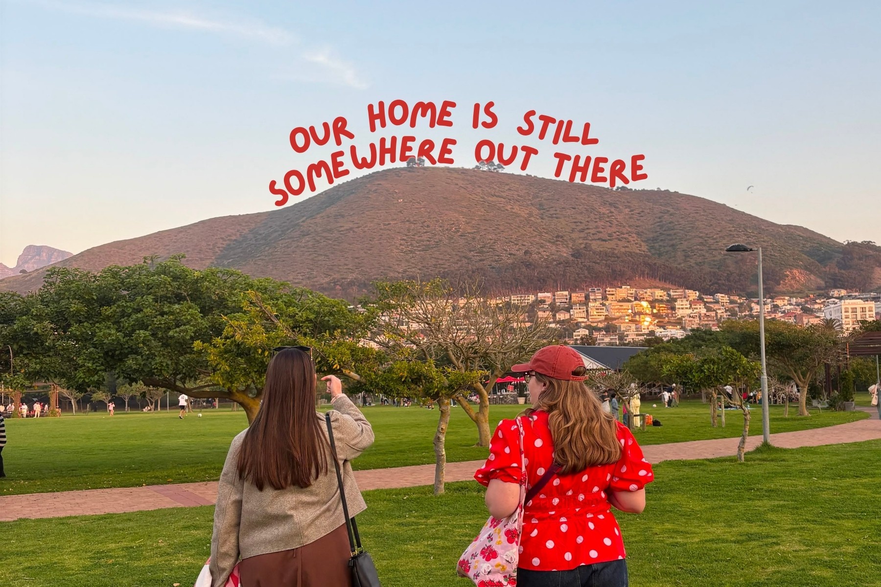 Two 25-year-old women walking in Green Point Park with text our home is still somewhere out there