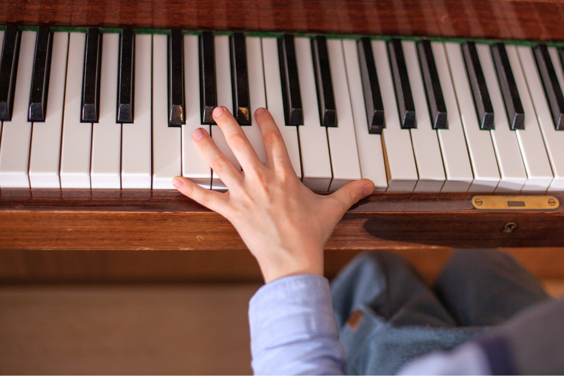 Child practising chords on an acoustic upright piano