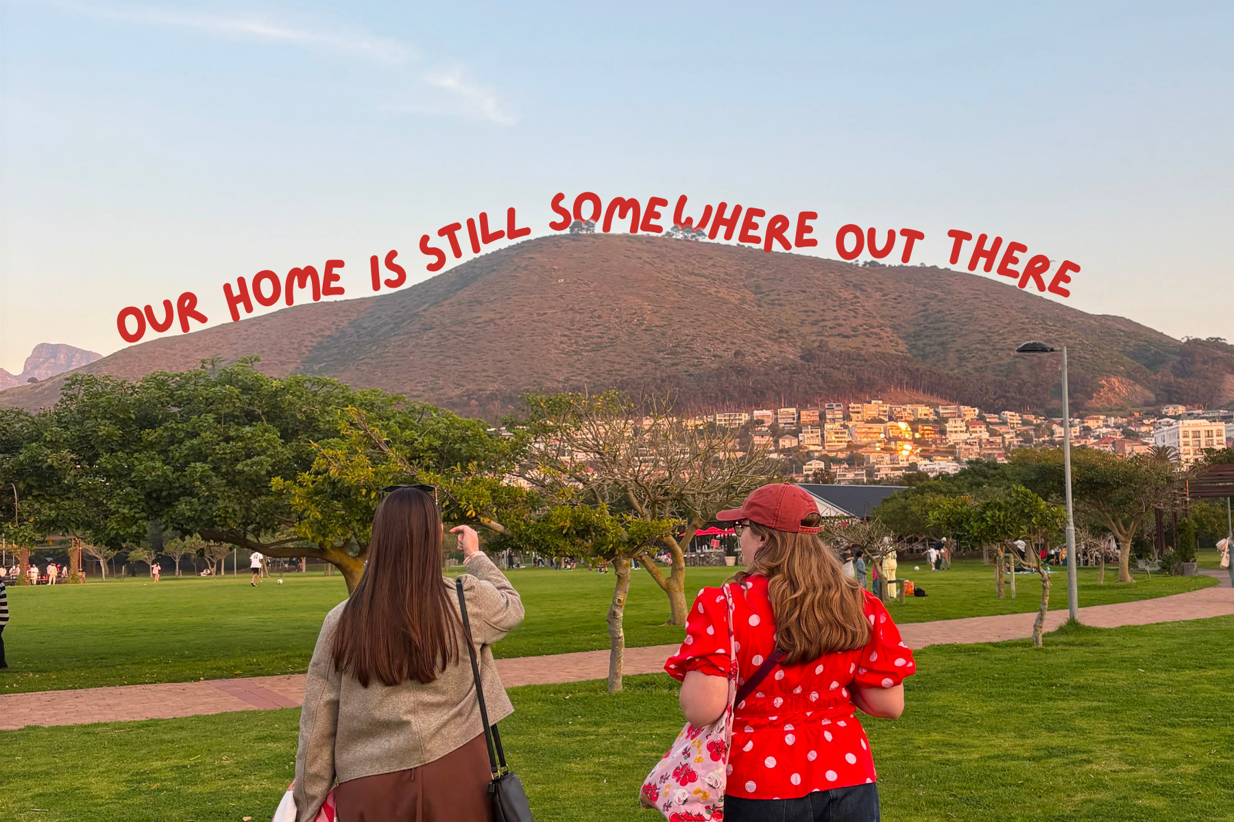 Two 25-year-old women walking in Green Point Park with text our home is still somewhere out there